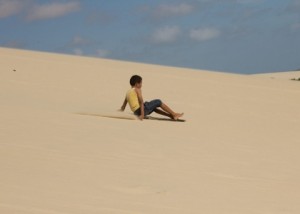 Foto com uma criança escorregando em uma montanha de areia.