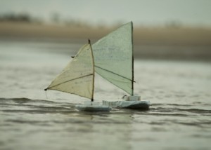 Foto com dois barcos a vela de brinquedos navegando sobre um lago.