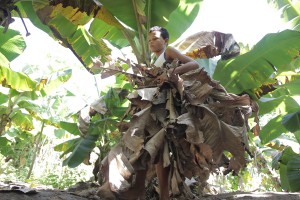 Foto de um garoto vestindo uma saia feita de folhas de bananeiras ressecadas.