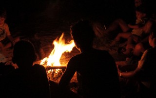 Foto com várias pessoas sentadas em volta de uma fogueira.