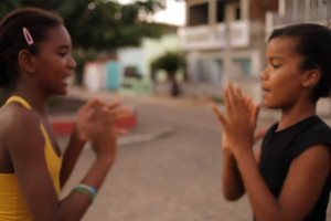Duas meninas negras brincando de adoleta em uma praça.
