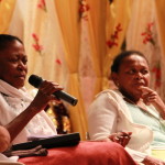 Foto ilustrando um diálogo entre pessoas, onde há  duas mulheres negras na imagem , onde a mulher da esquerda tem as mãos um microfone.