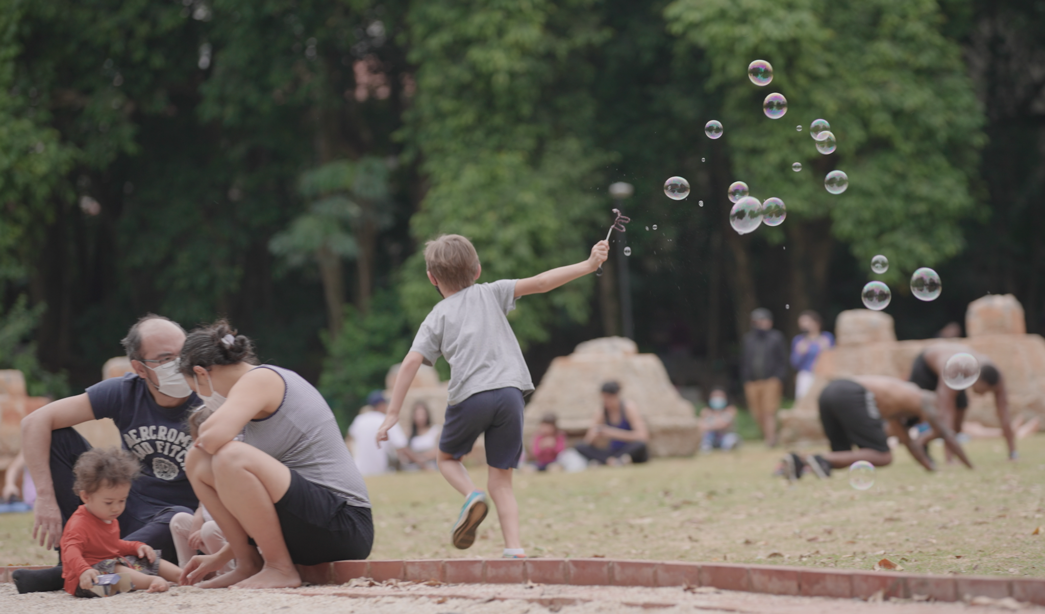 Menino corre em um parque e, em torno dele, há muitas bolhas de sabão.