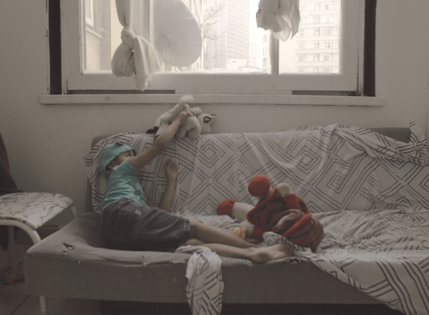 Menino está sentado em um sofá, brincando com seus bonecos.